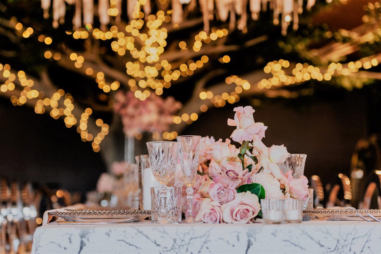 Pink flower boquets and glassware in front of fairy light backdrop
